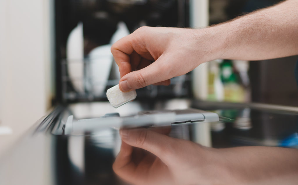 Man putting detergent tablet into dishwasher.